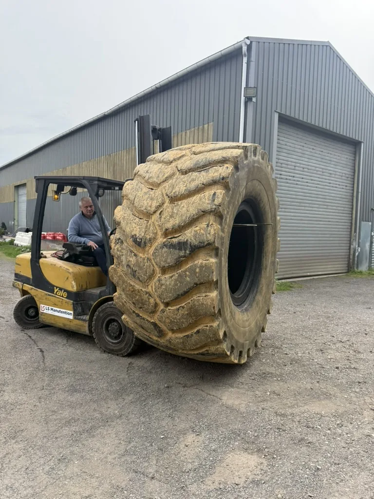 Pascal Ettinger manœuvrant un pneumatique de grande dimension avec un chariot élévateur devant l’atelier